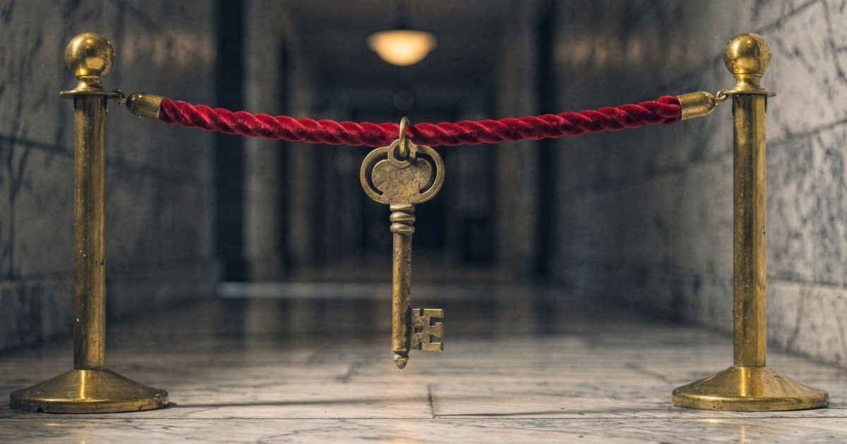 An old brass key on a red velvet rope barrier in a dim marble hallway, soft warm light