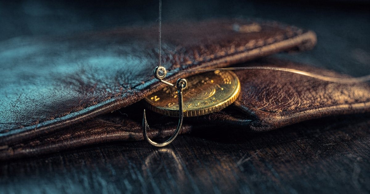 A small steel fishing hook on a thin line slipping into an open brown leather wallet on a dark wooden desk, a gold coin half out of the wallet