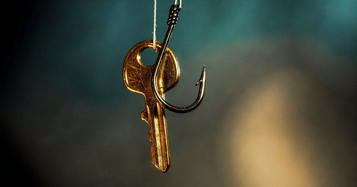 A small brass key hanging from a steel fishing hook against a dark background